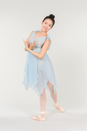 站立在古典芭蕾姿势的透明浅兰的礼服的年轻亚裔芭蕾舞女演员