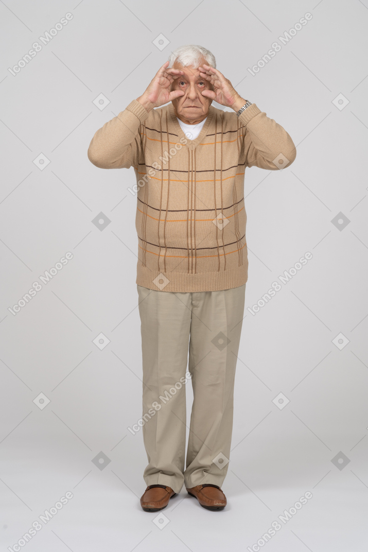 一位穿着休闲服的老人透过手指看的正面图