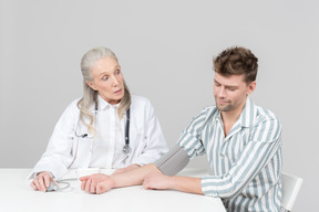 Envelhecido médico feminino verificando a pressão arterial de um jovem