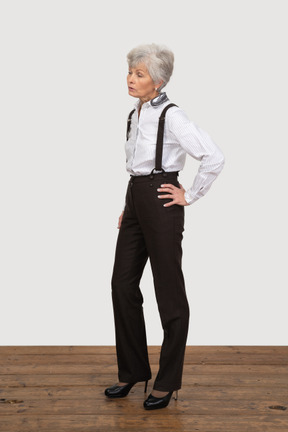 Vue de trois quarts d'une vieille dame mécontente en vêtements de bureau mettant les mains sur les hanches