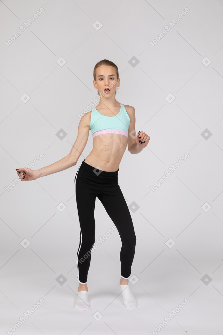 Vista frontal de una jovencita en ropa deportiva gesticulando mientras baila