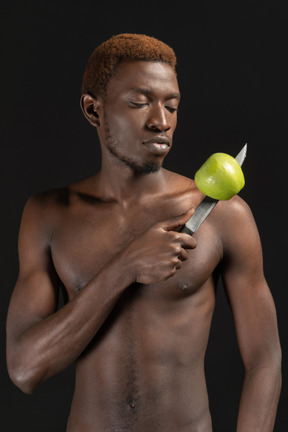 Un joven musculoso sosteniendo un cuchillo con una manzana verde