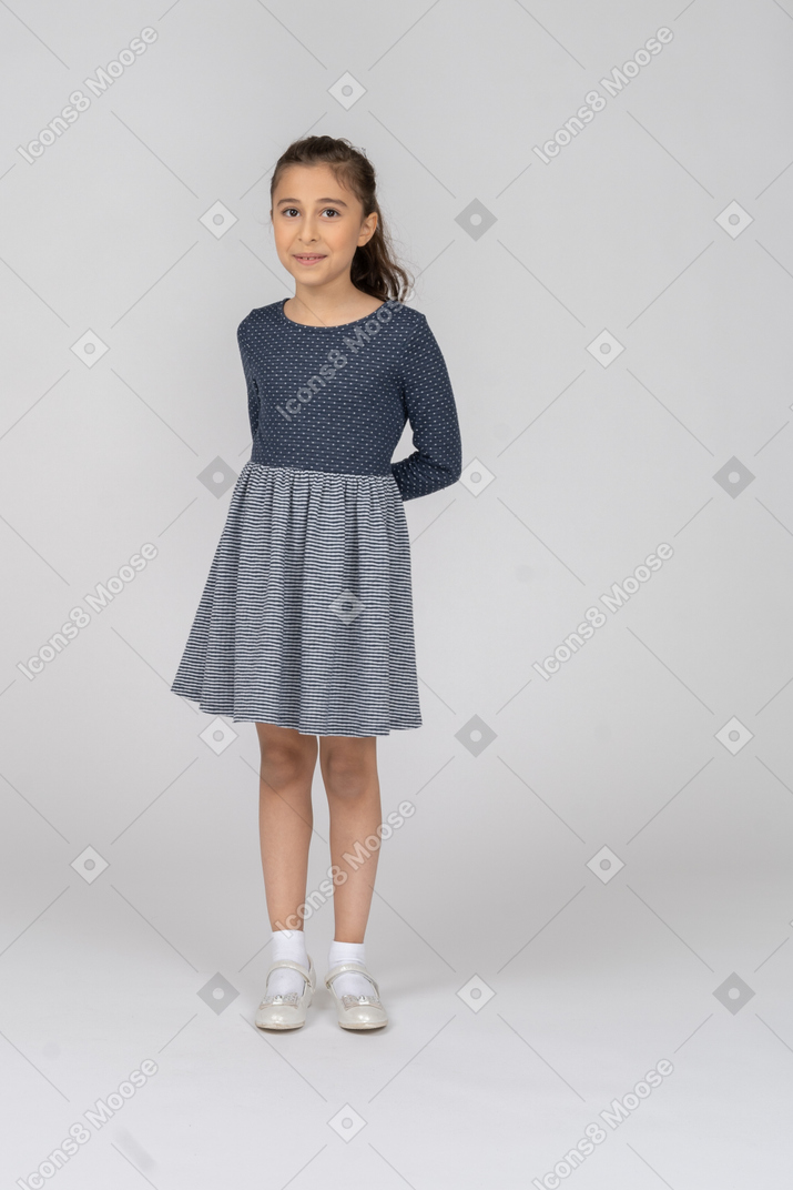Vista frontal de una niña escondiendo las manos detrás de su espalda con una sonrisa tímida