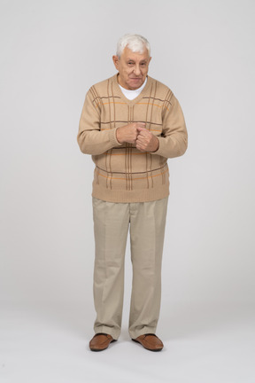 Front view of an old man in casual clothes standing with clenched fists and looking at camera