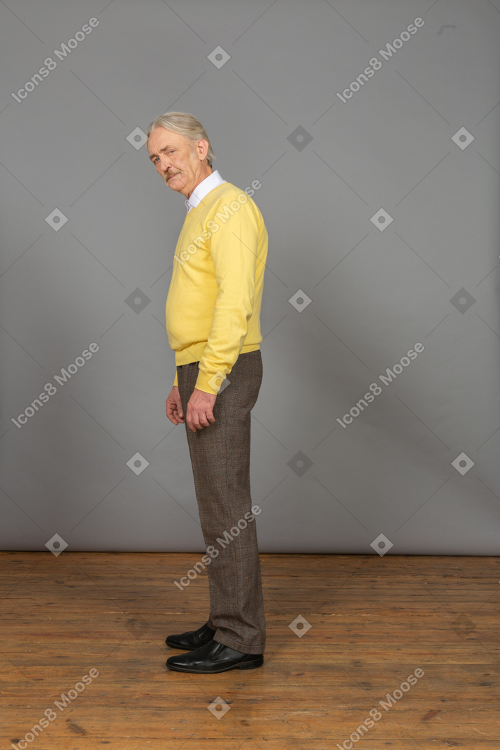 Vista lateral de um velho vestindo um pulôver amarelo se curvando e olhando para a câmera