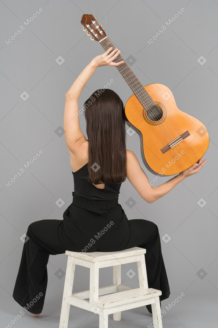 Young woman holding guitar above head