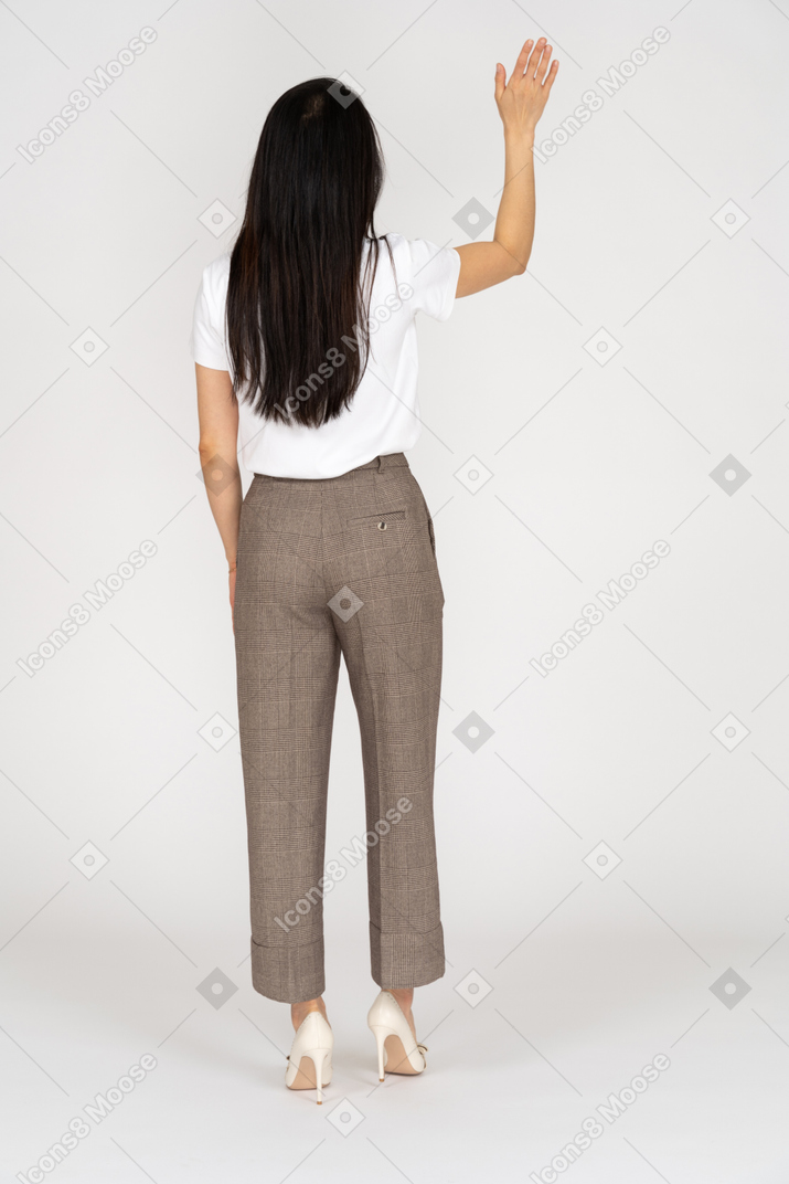 Vista posteriore di una giovane donna in calzoni alzando la mano