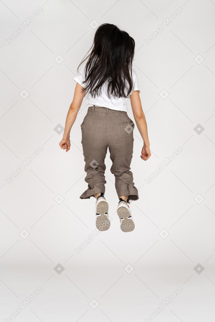 Vista traseira de uma jovem saltitante de calça e camiseta dobrando os joelhos