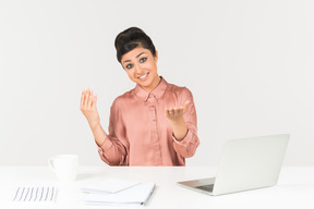 Young indian office worker sitting at the desk and like pointing forward