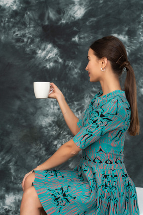A woman  in blue dress invites for a cup of tea
