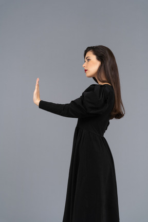 一位年轻的女士，穿着黑裙子举起她的手的侧视图