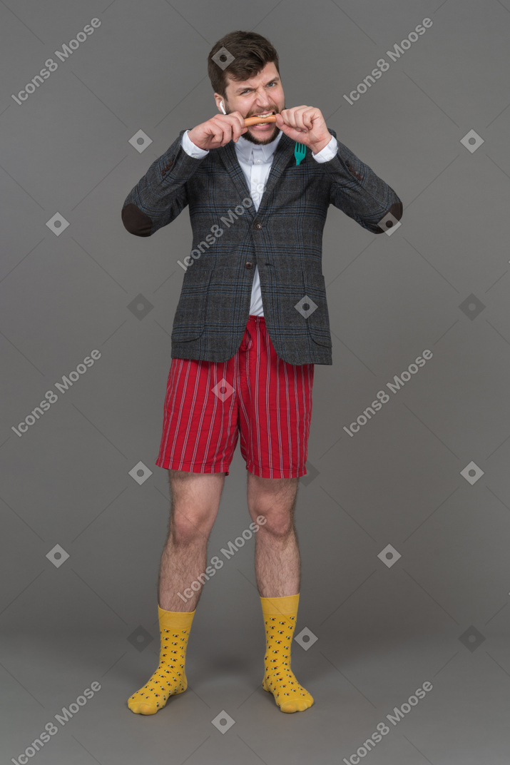 Young man in red shorts eating a sausage