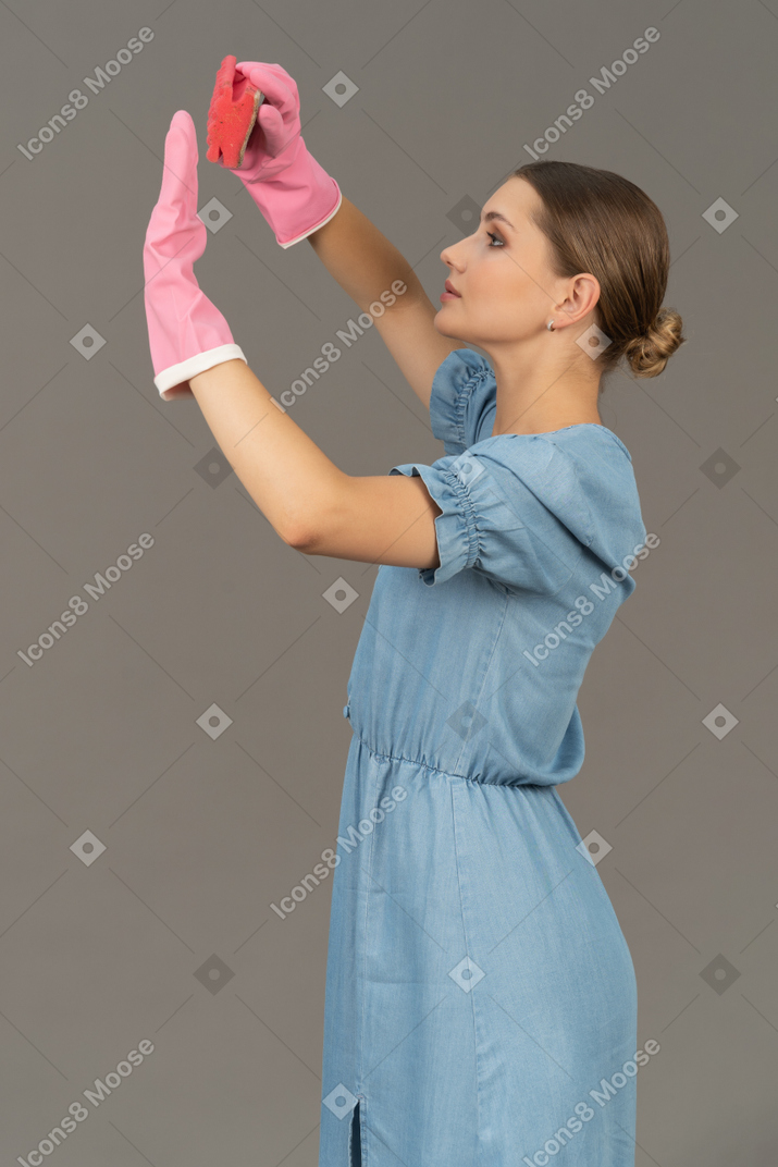 Side view of a young woman raising her gloved hands while holding a sponge