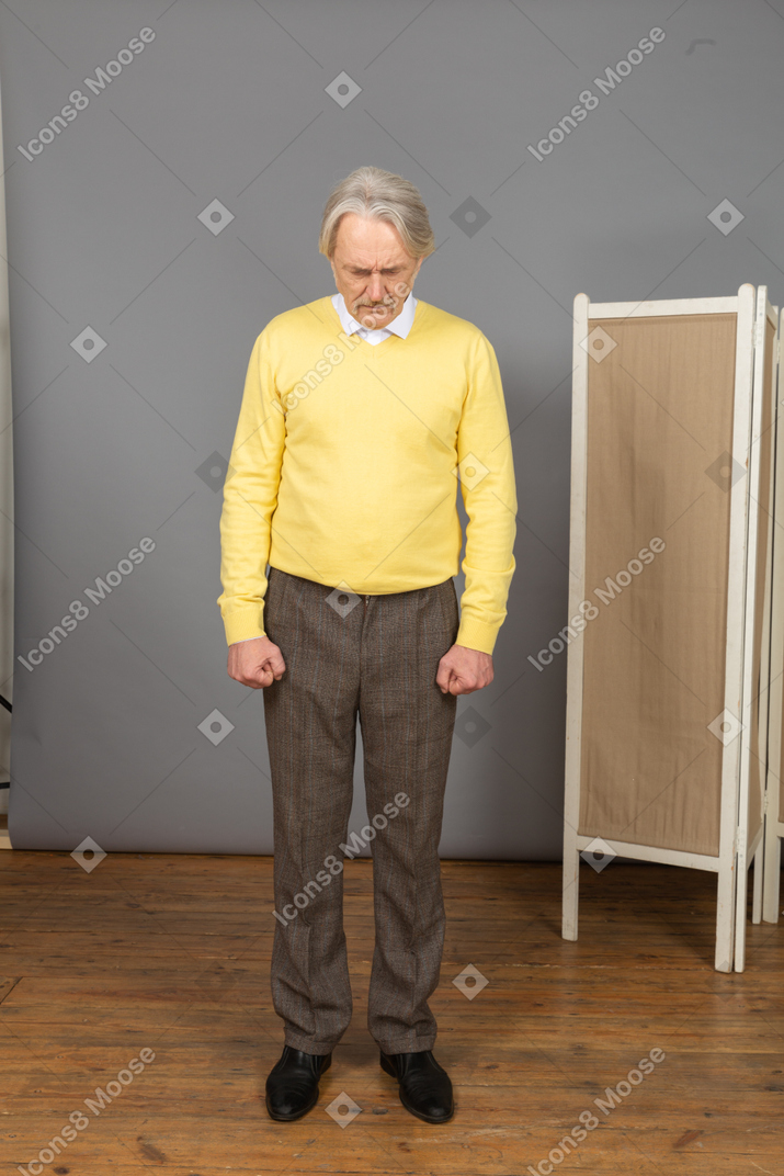 Front view of a depressed old man clenching fists while looking down