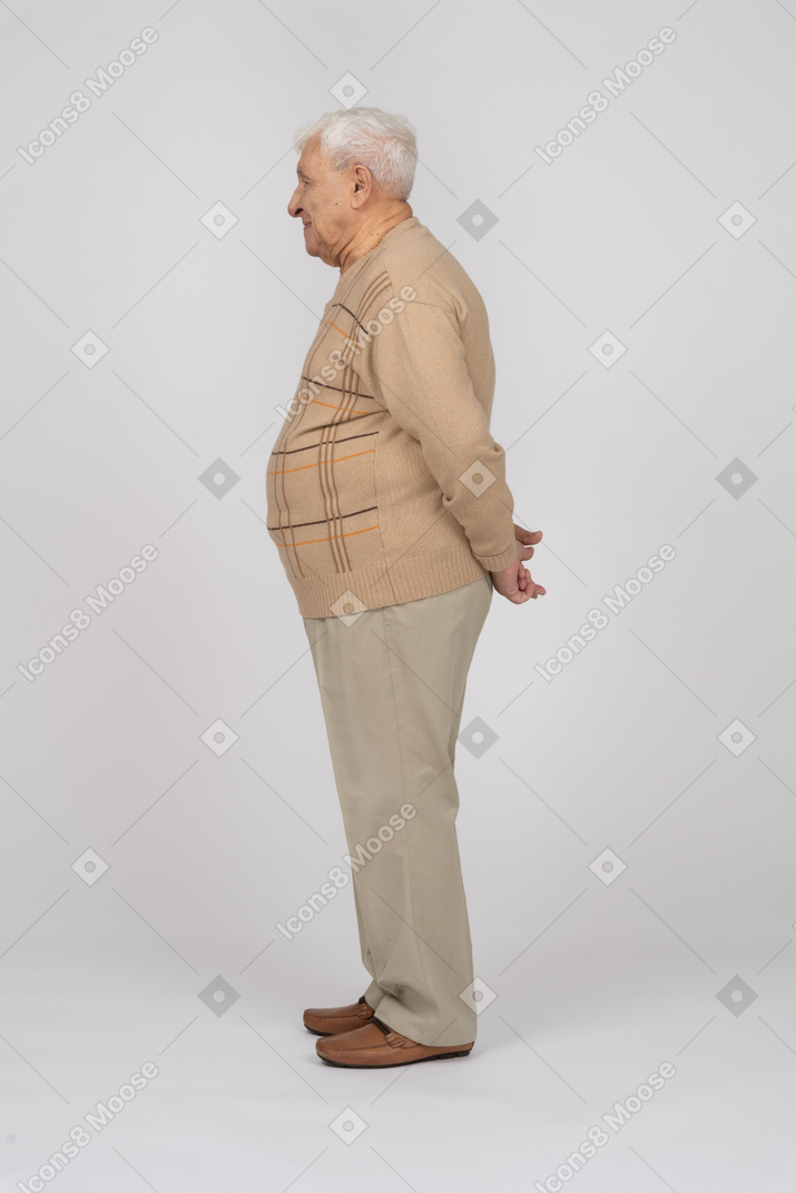 Vista lateral de um velho em roupas casuais em pé com as mãos atrás das costas