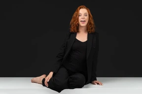 A frontal view of the cute red haired girl dressed in black and sitting on the white table