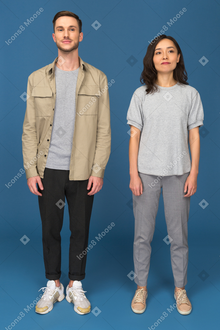 Young man and woman standing still in front of camera