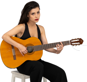 Front view of a sitting young lady in black suit playing guitar