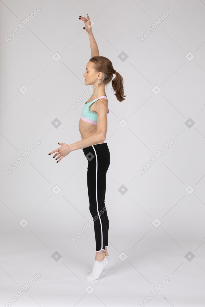 一个青少年的女孩，在运动服举起手，standing着脚尖的侧视图