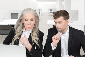 A man and a woman sitting at a table looking at a laptop