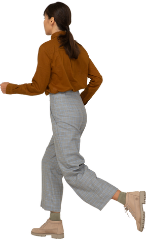 Vista posteriore di tre quarti di una giovane donna asiatica in corsa in calzoni e camicetta