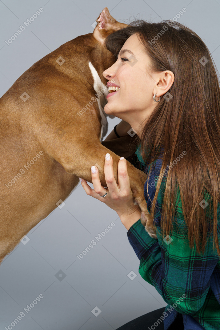 Vista lateral de uma mulher sorridente em camisa xadrez abraçando seu bulldog