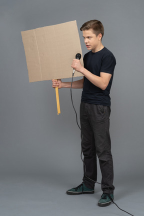 Junger mann, der in ein mikrofon spricht und ein plakat hält