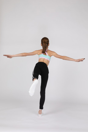 Back view of a teen girl in sportswear balancing on her leg