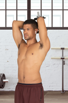 A shirtless man holding a barbell in a gym