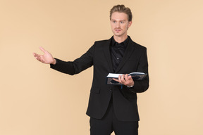 A white man in a fully black suit holding the quran