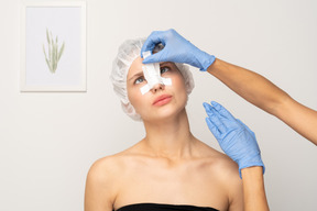 Doctor applying bandage to young woman's nose