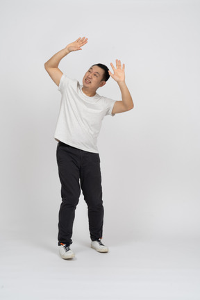 Front view of scared man standing with raised hands and looking up