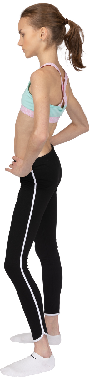 Vista lateral de una jovencita en ropa deportiva poniendo las manos en las caderas