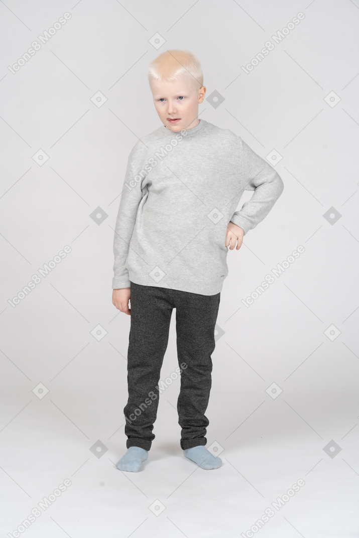 Front view of a  thoughtful kid boy opening mouth and putting hand on hip