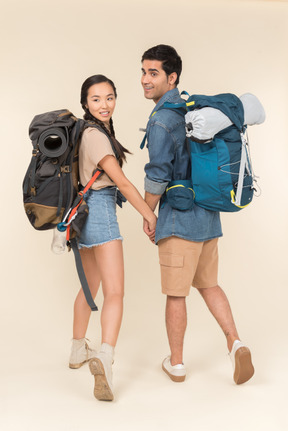 Young woman and man with huge backpacks holding hands and looking back