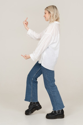 Side view of a blonde female stepping forward and showing middle finger on both hands