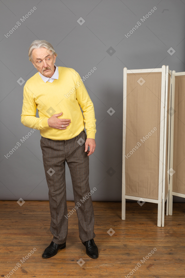 Vista frontal de un anciano poniendo la mano sobre el estómago mientras se inclina hacia adelante