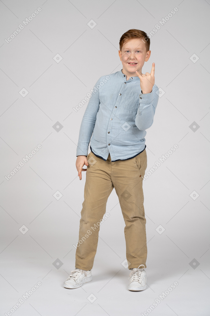 Front view of a happy boy making rock gesture and looking at camera