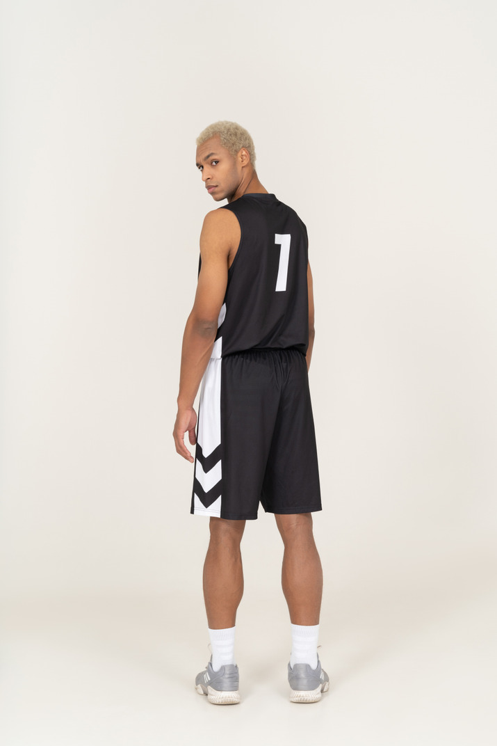 Back view of a suspicious young male basketball player turning head & looking at camera