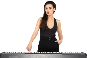 Vista frontale di una giovane donna in abito nero premendo il tasto di un pianoforte