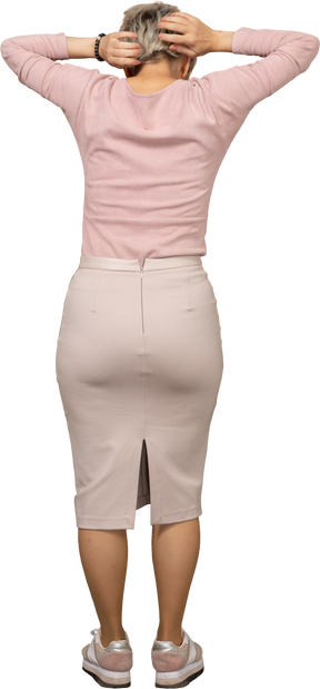 Rear view of a woman in casual clothes standing with hands behind head