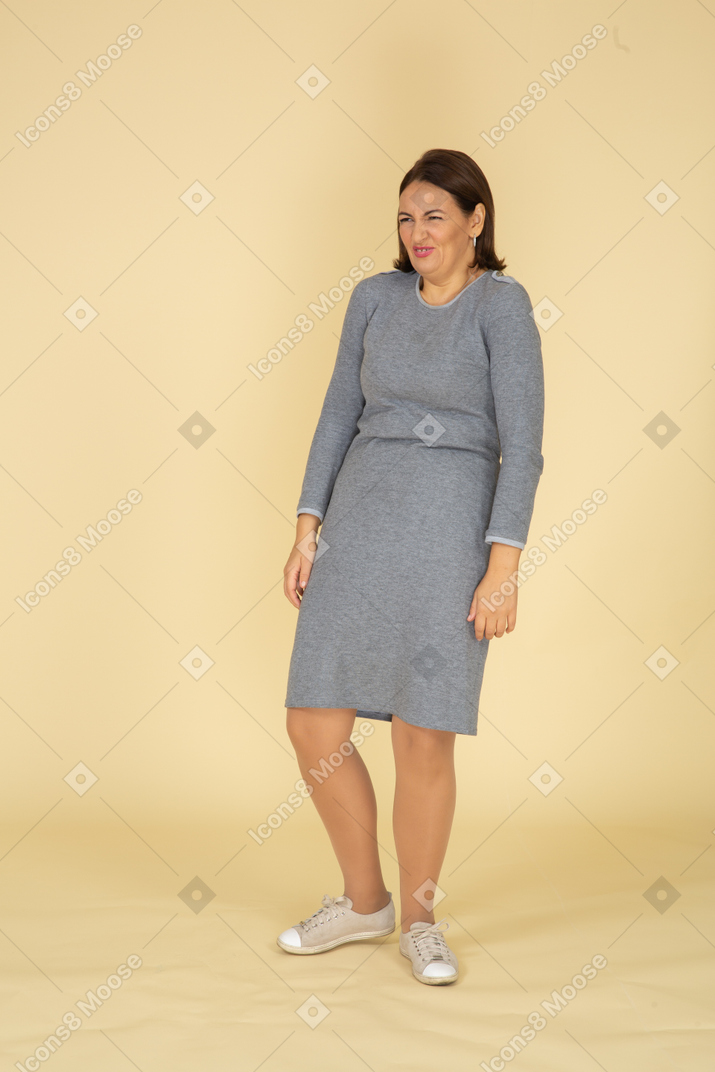 Vue de face d'une femme en robe grise faisant des grimaces