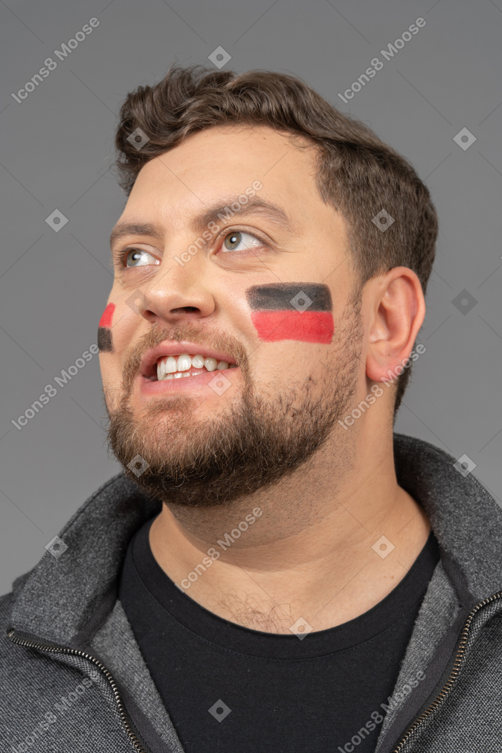 Трехчетвертный вид улыбающегося футбольного фаната мужского пола с красочным фейс-артом