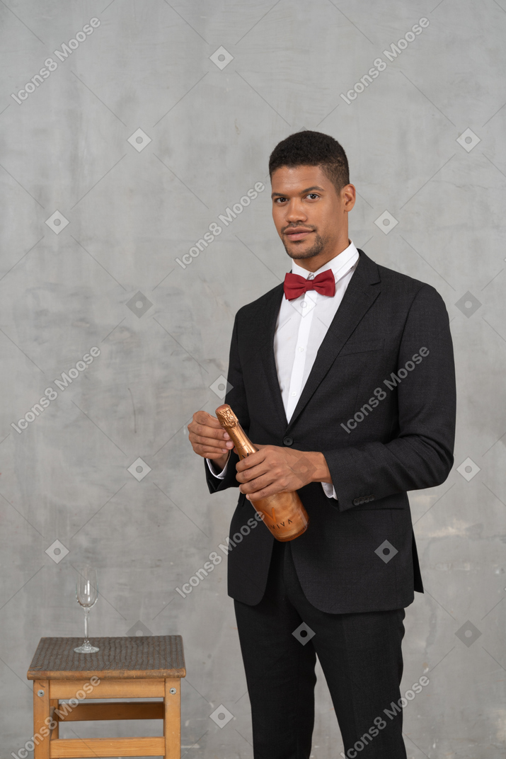 Young man opening a champagne bottle and looking at camera