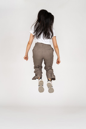 Vista posterior de una señorita saltando en calzones y camiseta doblando las rodillas