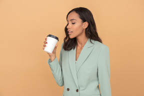 Séduisante jeune femme d'affaires à la recherche de la tasse de café qu'elle tient