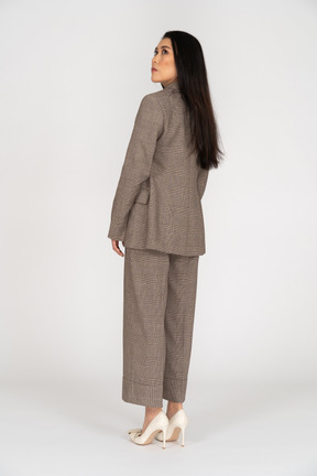 Three-quarter back view of a young lady in brown business suit looking up
