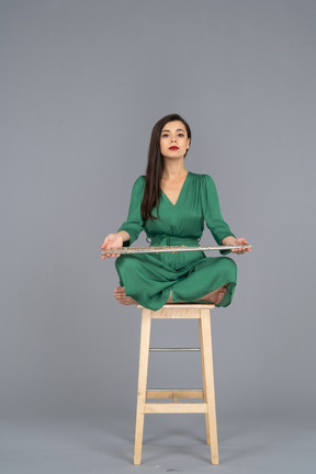 Pleine longueur d'une jeune femme tenant sa clarinette sur ses genoux alors qu'elle était assise sur une chaise en bois