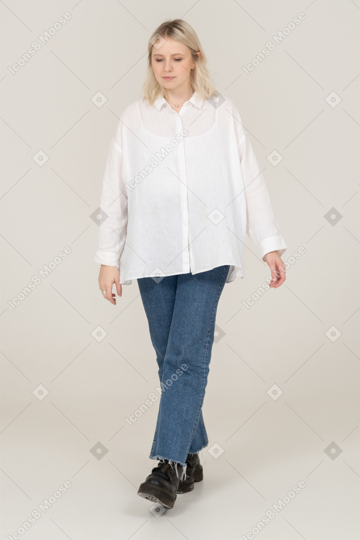 Vista frontale di una donna bionda carina in abiti casual, guardando verso il basso e facendosi avanti