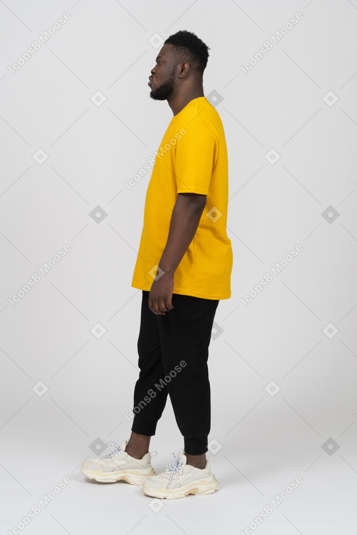 一个穿着黄色 t 恤、站着不动、撅嘴的黑皮肤年轻男子的侧视图